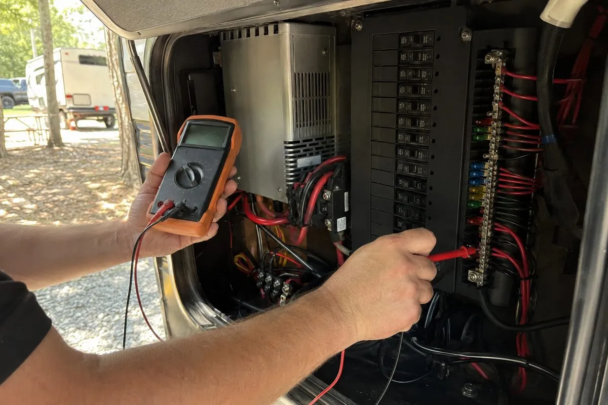 Technician testing an RV 12-volt converter and breaker panel with a multimeter at a campground